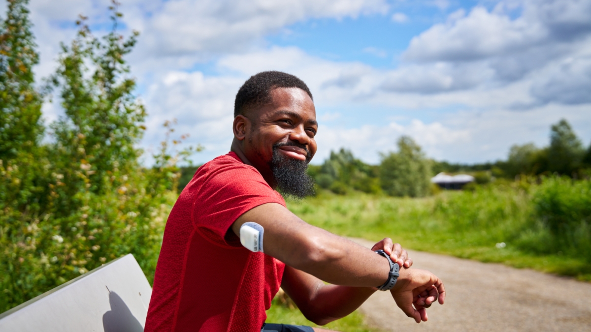 Man with a red shirt sitting on a bench with an Omnipod Pod on his right arm