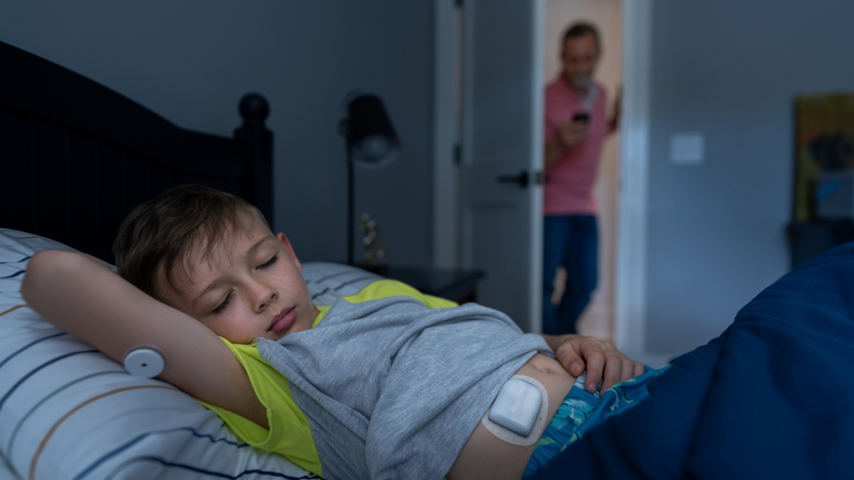 A boy sleeping in bed with dad standing at the door