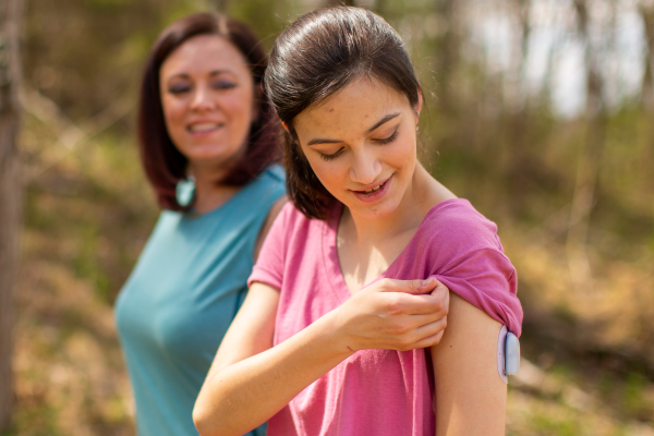 Podder Gracie pulling up her sleeve to show her Pod on her left arm while her mother is standing behind her