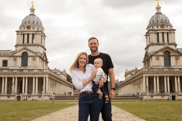 Two parents with the mom holding their baby standing in front of an old building for a photo
