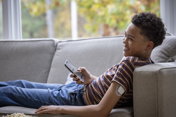 Young boy laying down on a couch with a Pod on his left arm