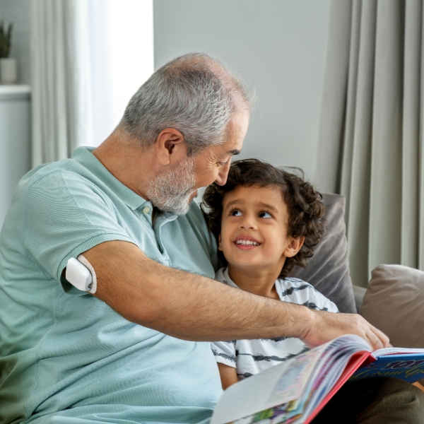 Man with an Omnipod Pod on his right arm, sitting on a couch with a boy reading a book